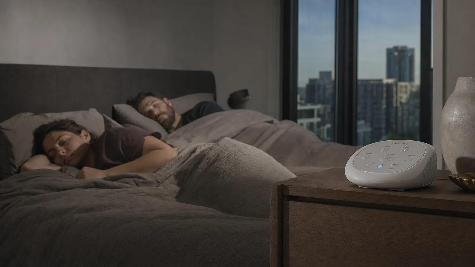 Couple sleeping peacefully in a city apartment with a sound machine on the dresser