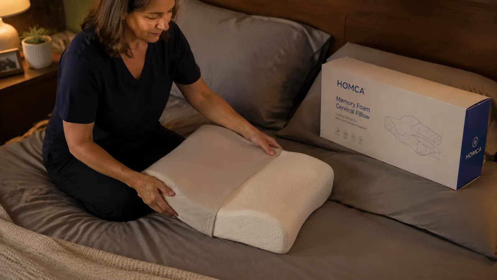 A woman adjusting a cervical contour pillow on her side before sleep, bedroom lamp on low