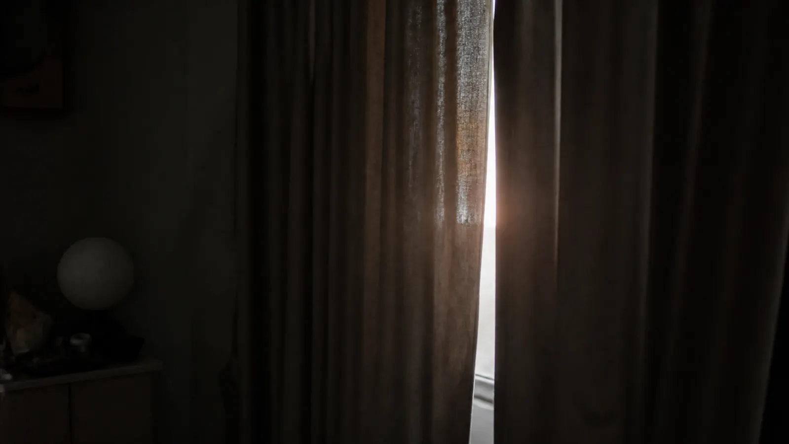 Bedroom window with light leaking through curtain gap at night, showing the problem of uncontrolled light
